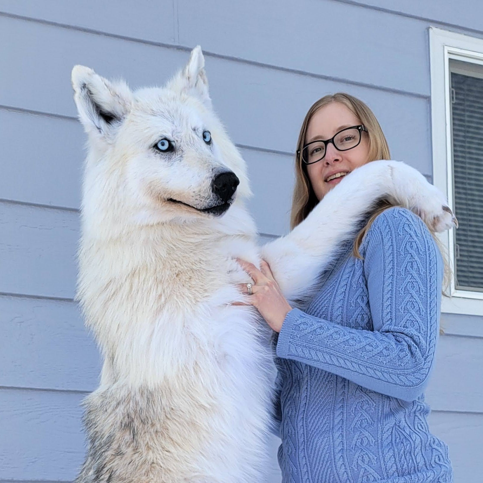 Woman standing next to a large white dog on a snowy ground.