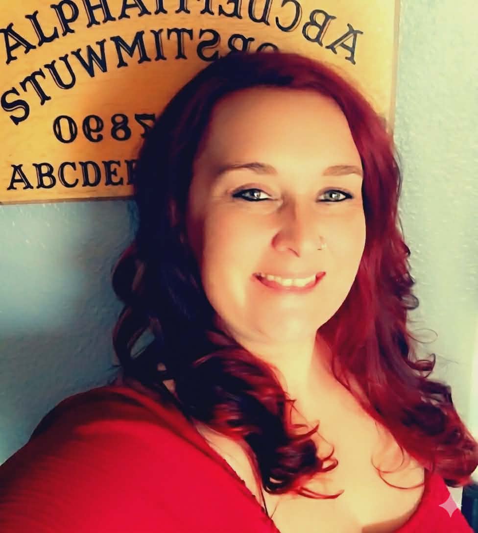 Woman with red hair smiling in front of a wall with letters and numbers.